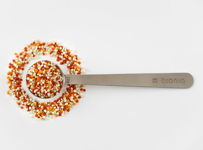 Spoonful of Bioniq granules above an open supplement jar